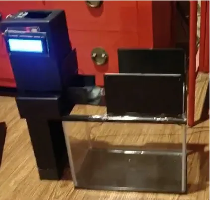 Automatic fish feeder unit with its LCD lit, mounted beside the aquarium